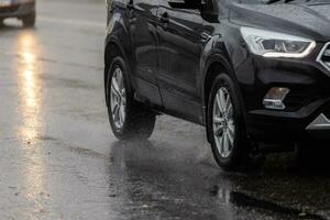 les éclaboussures d'eau de pluie s'écoulent des roues d'une voiture noire se déplaçant rapidement dans la ville de la lumière du jour photo
