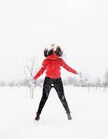 Jeune femme insouciante brune en pull rouge sautant dans la neige à l'extérieur photo
