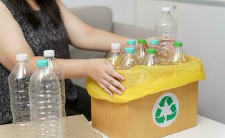 Accueil recycler éco vert zéro concept femme lancement vide Plastique bouteille dans recyclage poubelle avec Jaune des ordures Sacs à maison. photo