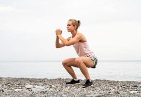 jeune femme sportive faisant des squats au bord de la mer photo