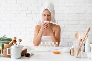 femme dans une serviette de bain blanche sentant la crème faisant des procédures de spa photo