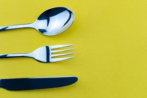 ensemble de fourchette, couteau et cuillère isolé sur fond de papier jaune. photo