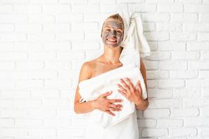 femme portant et tenant des serviettes de bain avec un masque facial en argile sur son visage photo