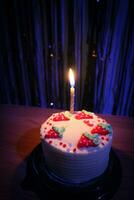 anniversaire gâteau avec arrose fraise et un bougies sur une bleu Contexte photo