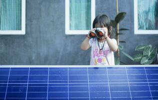 content asiatique fille admiratif solaire panneaux avec jumelles récemment installée à maison. photo
