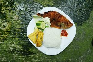 traditionnel asiatique nourriture, frit tilapia avec Frais des légumes sur blanc assiette sur béton Contexte photo