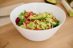 encore la vie avec une blanc bol de Frais salade avec biologique légumes, Avocat fruit et légumes verts sur une en bois table photo