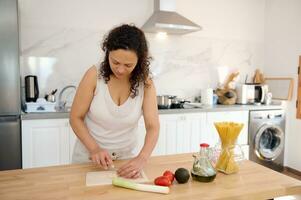 Latin américain femelle chef en train de préparer une en bonne santé salade pour dîner à maison, couper Ail sur une Coupe planche photo