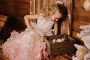 jolie fille dans une robe élégante rose regardant une boîte en bois avec des boules photo