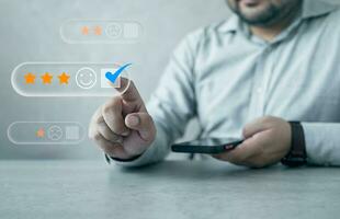 client pressage sur une visuel écran et en portant téléphone intelligent avec Trois étoiles icône et content visage pour retour d'information la revue la satisfaction un service photo