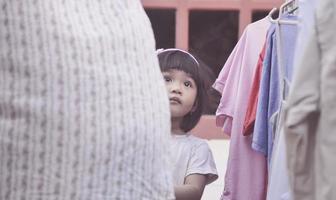 une petite fille accompagne sa mère en train de sécher des vêtements. photo