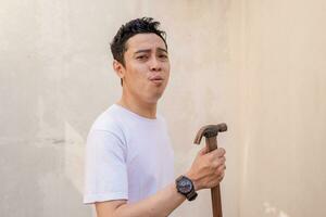 indonésien Hommes pose frappe, tenir le petit marteau et porter blanc T-shirt. photo