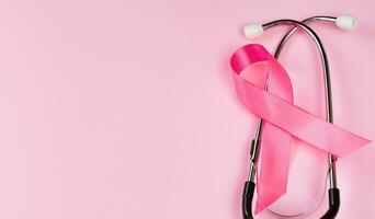 Mois de la sensibilisation au cancer du sein. ruban rose et stéthoscope sur fond coloré. concept de soins de santé des femmes. symbole de lutte contre l'oncologie. photo