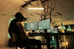 Masculin pirate travail à pirater serveur avec vr 3d casque, Planification cyber-attaque avec virtuel réalité à nuit. Jeune adulte causant ordinateur logiciels malveillants, en utilisant interactif lunettes, cyber-terrorisme. photo