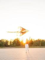 Jeune femme faisant voler un cerf-volant dans un parc public au coucher du soleil