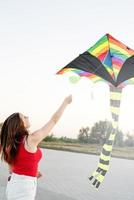 Jeune femme faisant voler un cerf-volant dans un parc public au coucher du soleil photo