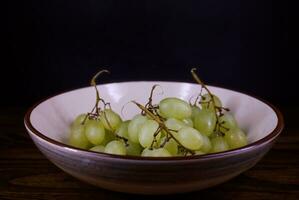 une petit magnifique bouquet de mûr vert les raisins dans une Profond céramique plaque. photo