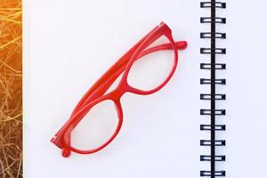 lunettes rouges sur un cahier vierge ouvert dans le champ avec la lumière du soleil photo