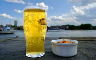 Bière et Patate puces. verre de blond Bière avec peu mousse. frites dans blanc bol bien pour casse-croûte à un Extérieur pub sur le bord de rivière. photo