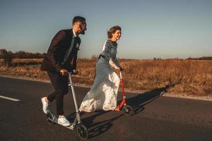 couple de mariage souriant chevauchant un scooter le long de la route au coucher du soleil photo