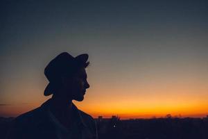 silhouette d'un portrait d'homme avec chapeau regardant le coucher du soleil sur la ville photo