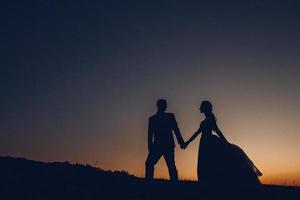 silhouette du couple de mariage main dans la main sur fond de coucher de soleil photo