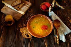 tomate soupe dans une argile assiette sur une en bois ancien ferme table près une pièce de marron pain. photo