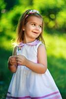 magnifique fille souriant et en portant une fleur trèfle. une petit enfant sur une Contexte de vert des buissons. photo