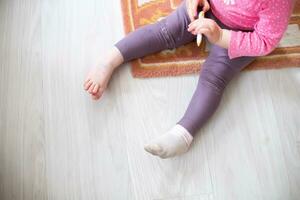 une fille sans pour autant un chaussette est assis sur le sol. le jambes de le enfant qui a pris de le sien chaussette. photo