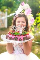 fille en portant anniversaire gâteau avec nombre 8 et une inscription content anniversaire. célébrer cérémonial événements sur rue pendant quarantaine. enfant dans Contexte décoré photo zone de fleurs.