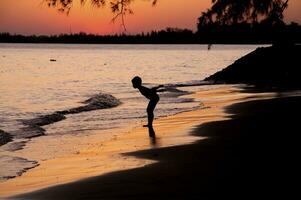 silhouette de garçon permanent sur le plage à le coucher du soleil photo
