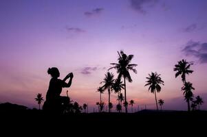 silhouette de une femme prise une photo de paume des arbres à le coucher du soleil