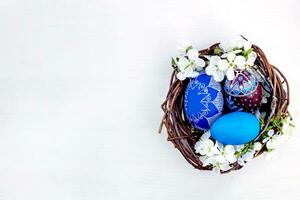 nid avec Pâques des œufs et branches de printemps floraison cerises sur une blanc en bois Contexte. des œufs peint avec Naturel colorants. printemps religieux vacances concept. photo