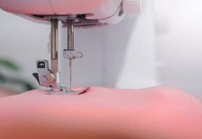 proche en haut de couture machine travail avec rose tissu, point Nouveau vêtements. photo