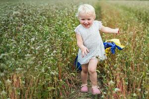 le drapeau de Ukraine est dans le mains de une enfant à la recherche en haut. ukrainien fille dans une champ de épanouissement sarrasin. journée de l'ukraine incapacité. unité journée photo