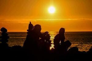 deux gens séance sur rochers à le coucher du soleil photo