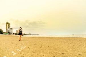 le voyageur se tient sur la plage de sable et regarde les gens nager photo