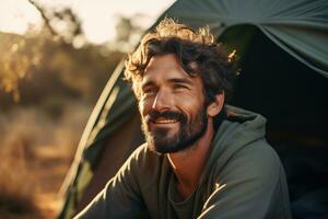 portrait de homme à la recherche à caméra tandis que près camping tente à le coucher du soleil ai généré photo