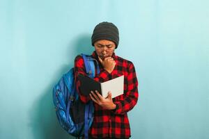 pensif Jeune asiatique étudiant homme est en pensant tandis que en portant livre et permanent contre bleu Contexte photo