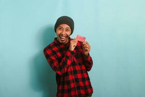 excité Jeune asiatique homme est en portant banque crédit cartes dans le sien mains, isolé sur bleu Contexte. photo
