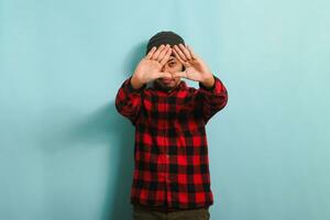 Jeune asiatique homme avec bonnet chapeau et rouge plaid flanelle chemise fabrication une Triangle geste avec palmiers, symbolisant le environnement protection, recyclage, et réutiliser concept, isolé sur une bleu Contexte photo