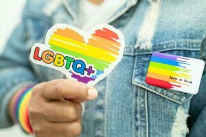 une dame asiatique portant des bracelets de drapeau arc-en-ciel et tenant un coeur rouge, symbole du mois de la fierté lgbt célèbre chaque année en juin les droits des gays, lesbiennes, bisexuels, transgenres et humains. photo