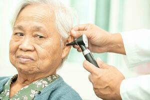 audiologiste ou ent médecin utilisation otoscope vérification oreille de asiatique Sénior femme patient traiter audition perte problème. photo