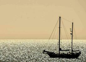 une voilier est vu dans le océan à le coucher du soleil photo