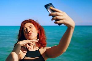 femme rousse prend selfie sur l'appareil photo du smartphone