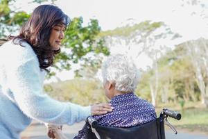 aider et soigner une femme âgée asiatique assise sur un fauteuil roulant dans un parc. photo