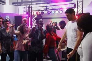 de bonne humeur Jeune gens dansant ensemble à social rassemblement dans boîte de nuit. content Hommes et femmes foule aller en boîte et faire la fête sur piste de dance tandis que assister discothèque dans club photo