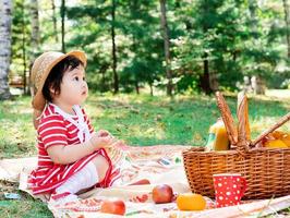 mignon petit bébé dans une robe rouge et un chapeau srtaw sur un pique-nique dans le parc photo