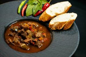 traditionnel hongrois nourriture du boeuf Goulache avec pain un épicé poivrons photo