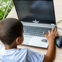 peu garçon séance à table en utilisant portable pour en ligne classe dans classe 1, enfant en train d'étudier sur portable de Accueil pour distance apprentissage en ligne éducation, école garçon les enfants mode de vie concept photo